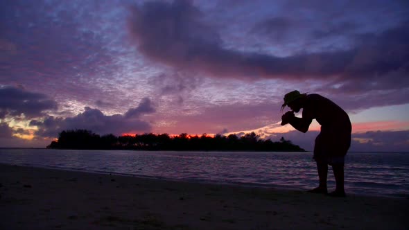 A local islander blows a conch shell during sunset on a scenic tropical island in Fiji.