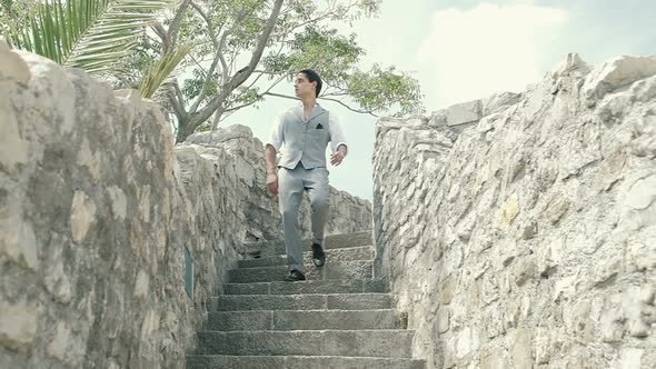 Attractive young fashion man in a suit runs down the stairs in an old fortress outdoor. Slow motion