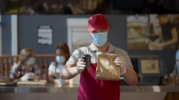 Young Man Worker Wearing Face Mask and Gloves Giving Take Away Meal To Customer