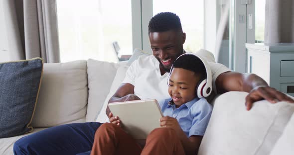 African american father and son using a digital tablet together with boy wearing headphones