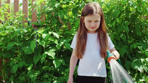 Girl Smiling Watering Beds in Garden with Hose