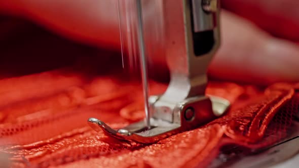 Steel part of sewing machine with a needle working on red cloth. 