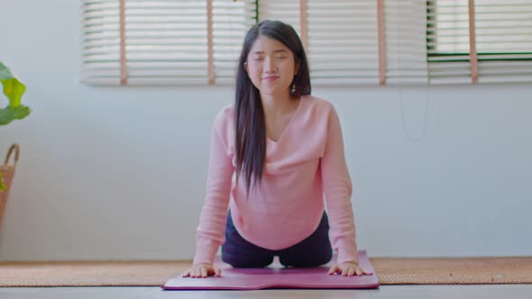 Asian woman in casual doing yoga Cobra pose at home