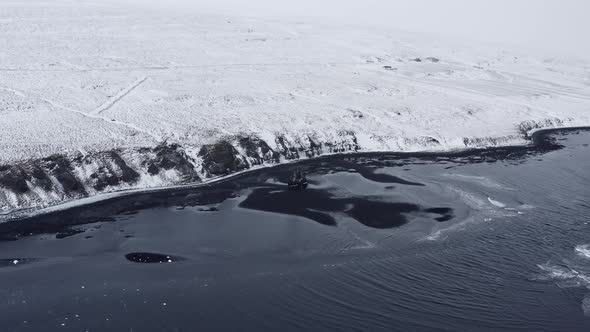 Drone Over Low Tide On Black Sand Beach Towards Snowy Landscape