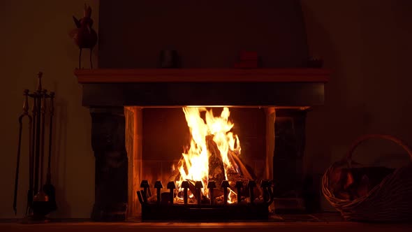 A 4k clip of a fire burning in a fireplace. On the right is a basket with more peaces of wood. This