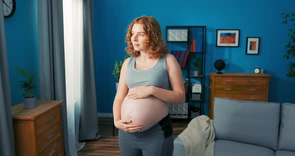 Closeup on Profile of Standing Pregnant Woman Living Room Scenery Girl Dreamily Touches Her Belly