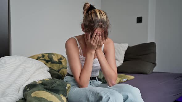 Crying teenage girl sitting depressed on bed