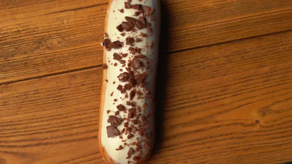 Top View of a Sweet Eclair with Chocolate Sprinkles Rotating on a Wooden Table on a Blue Background