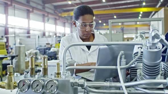 African Female Engineer Operating Industrial Machine with Laptop