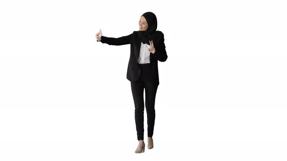 Smiling Arab Woman in Hijab Taking Selfies on Her Mobile Phone As She Walks on White Background.