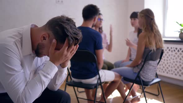 Sad Man Crying and Covers Face with Hands on Group Therapy Session on Background of People Sitting