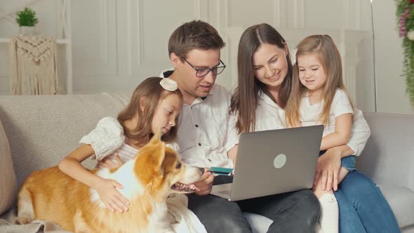 A Happy Family Uses a Laptop for Online Shopping, Sitting on the Couch at Home.