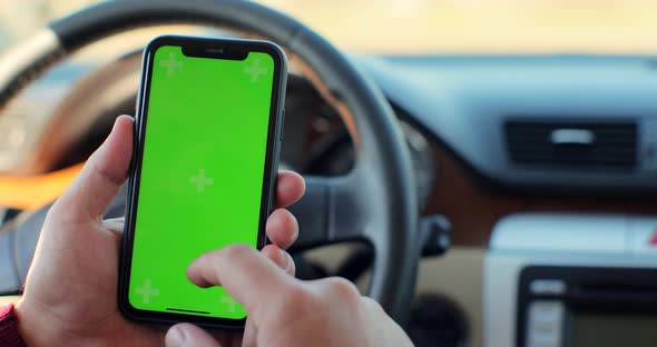 Man Hand Using Chromakey Mobile Phone with Empty Green Screen in Modern Car