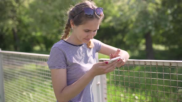 Attractive Young Woman Uses Smatphone in Park at Day