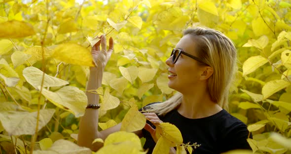 Portrait Young Smiling Blonde Girl in Glasses and T-shirt, She Is in the Bushes of Yellow Leaves.