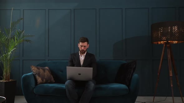 Portrait of an Elegant Businessman Sitting with Laptop on the Couch at the Luxury Blue Office