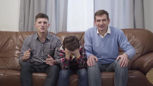 Portrait of Three Men of Different Ages Watching Football Match on TV and Gesturing. Sad Caucasian