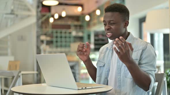 Upset African Man Reacting to Loss on Laptop in Cafe