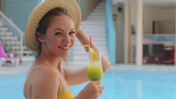Happy Carefree Millennial European Fair Skinned Girl in Swimsuit and Hat Relaxing in Pool with Glass