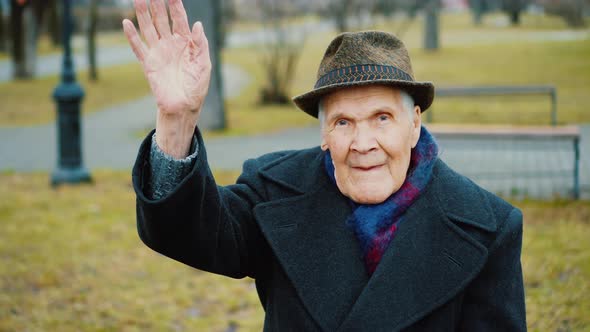 Old senior man waves his hand, greets, says Hello, He is happy sitting in park