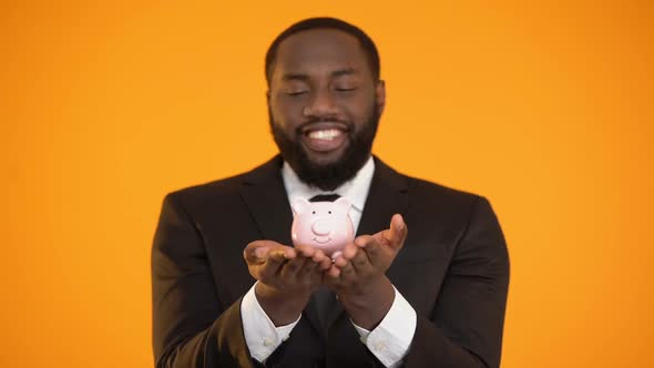 Cheerful Afro-American Businessman Holding Piggybank, Banking Services, Deposit