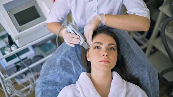 The Cosmetologist Makes the Procedure Ultrasonic Face Peeling of the Facial Skin of a Beautiful