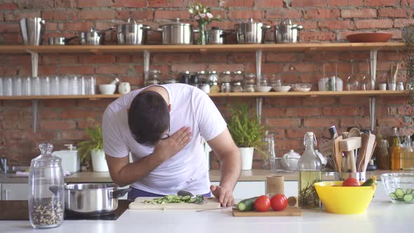 Young Man with Glasses Cuts Vegetables in the Kitchen and Experiences a Sharp Heartache