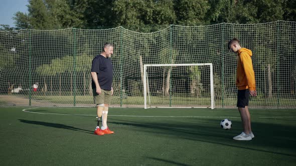 Wide Shot Positive Mature Amputee and Teenage Boy Playing Soccer in Slow Motion on Sunny Summer Day