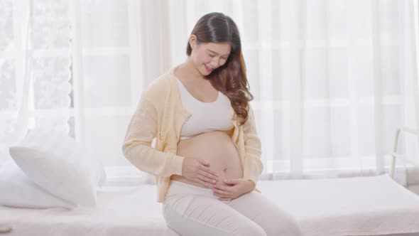 Happy Pregnant Woman sitting on bed holding and stroking her big belly at home