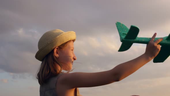 A Beautiful Blonde Teenage Girl in a Straw Hat in the Rays of the Setting Sun Plays with an Airplane