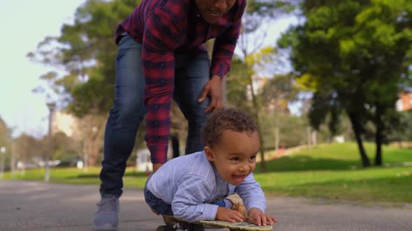 Boy Lying on Skateboard, Rolling To Camera with Help of Father 