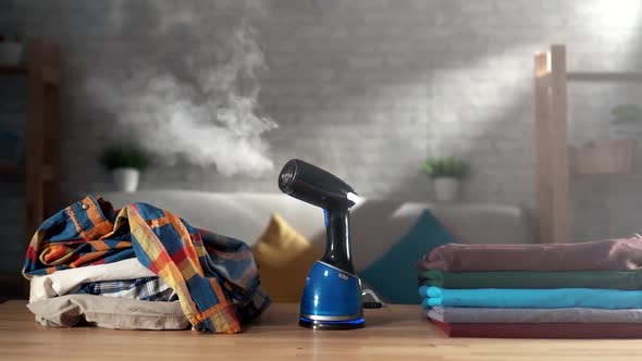 Portable Home and Travel Clothes Steamer on the Table Next To a Pile of Clothes