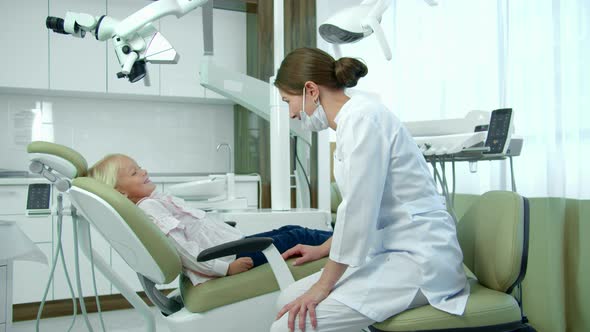 Female Dentist in Mask Talks To a Small Girl in Clinic.