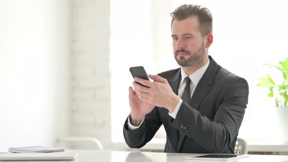 Attractive Young Businessman Using Smartphone in Office
