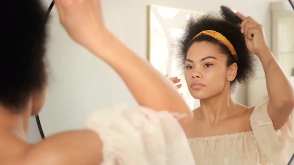 Black african american woman combing her hair with hairbrush, makes hairstyle