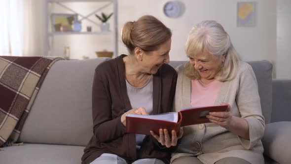 Senior Classmates Reviewing Photos From Past in Album, Laughing and Remembering