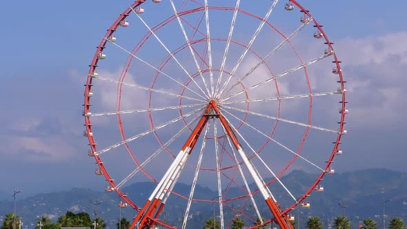 Ferris Wheel Against the Blue Sky with Clouds Near the Palm Trees in the Resort Town, Sunny Day