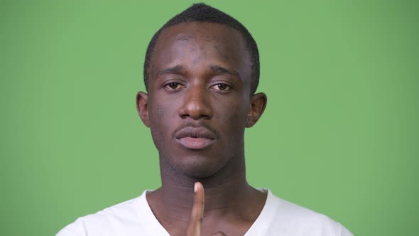 Young African Man with Finger on Lips Against Green Background