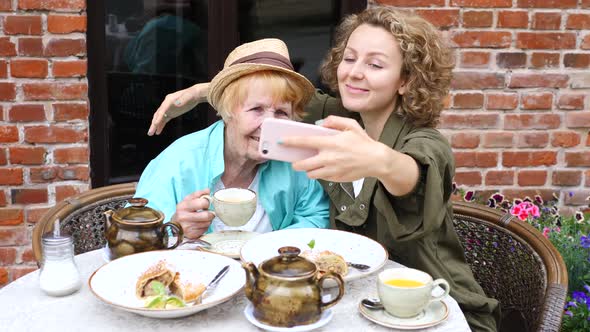 Grandmother And Granddaughter Taking Selfie With Smartphone In Cafe