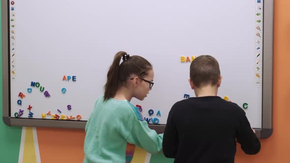 Two Children Compete to Form Words on a Magnetic Board During a Lesson in Class