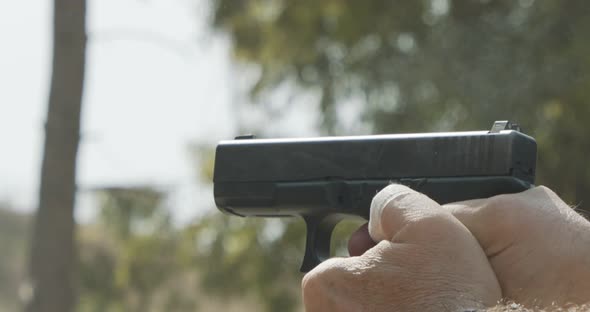 Slow motion of a man firing a hand gun in a firing range with cartridge flying away