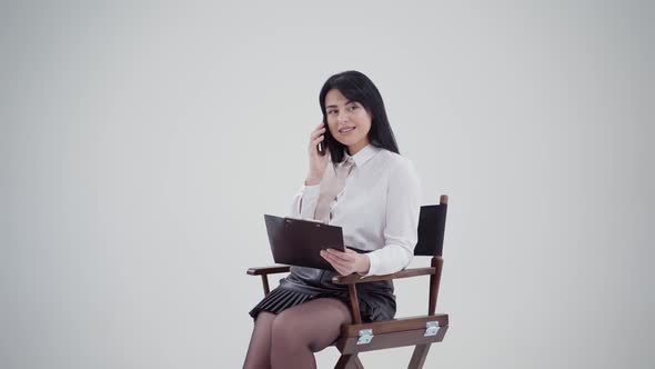 Brunette girl talking the phone isolated in studio. Young business woman in white blouse sitting in 