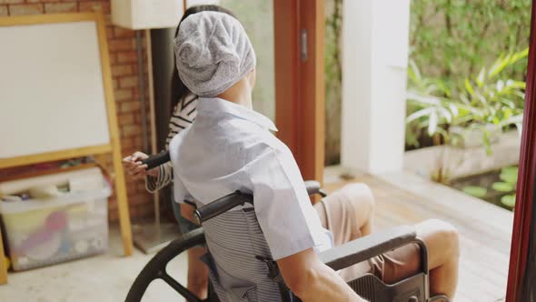 Old senior Asian man sitting in wheel chair in nusing home looking out of window