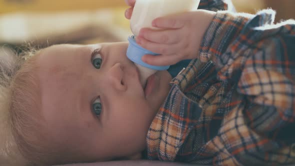 Funny Baby Eats Milk Mix From Plastic Bottle Lying on Bed