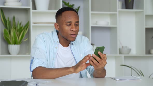 Young Mixed Race Man Sitting at Table, Reading Sms on Smartphone. Focused Millennial Businessman