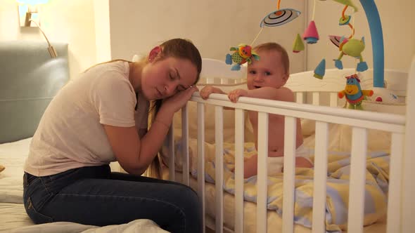 Little Baby Boy Shouting and Crying Next to Tired Mother Sleeping Next to His Crib