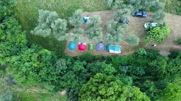 Top down ascending view of a camping site in a green field in Italy, with a man walking out