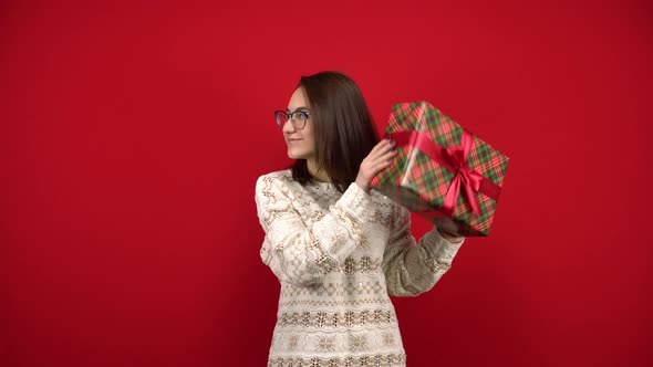 A Young Woman with Glasses Shakes a Christmas Present in Her Hands and Rejoices