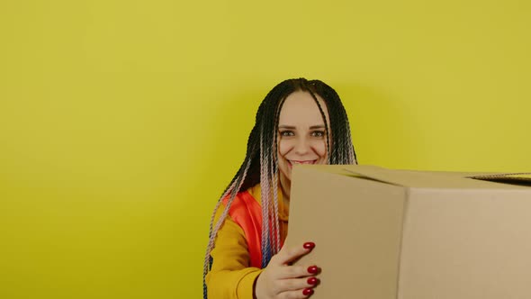 Young Woman in Vest with Cardboard Box on Yellow Background in Studio