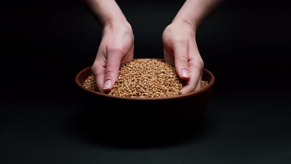 Taking Buckwheat in Hands From Bowl on Black Background